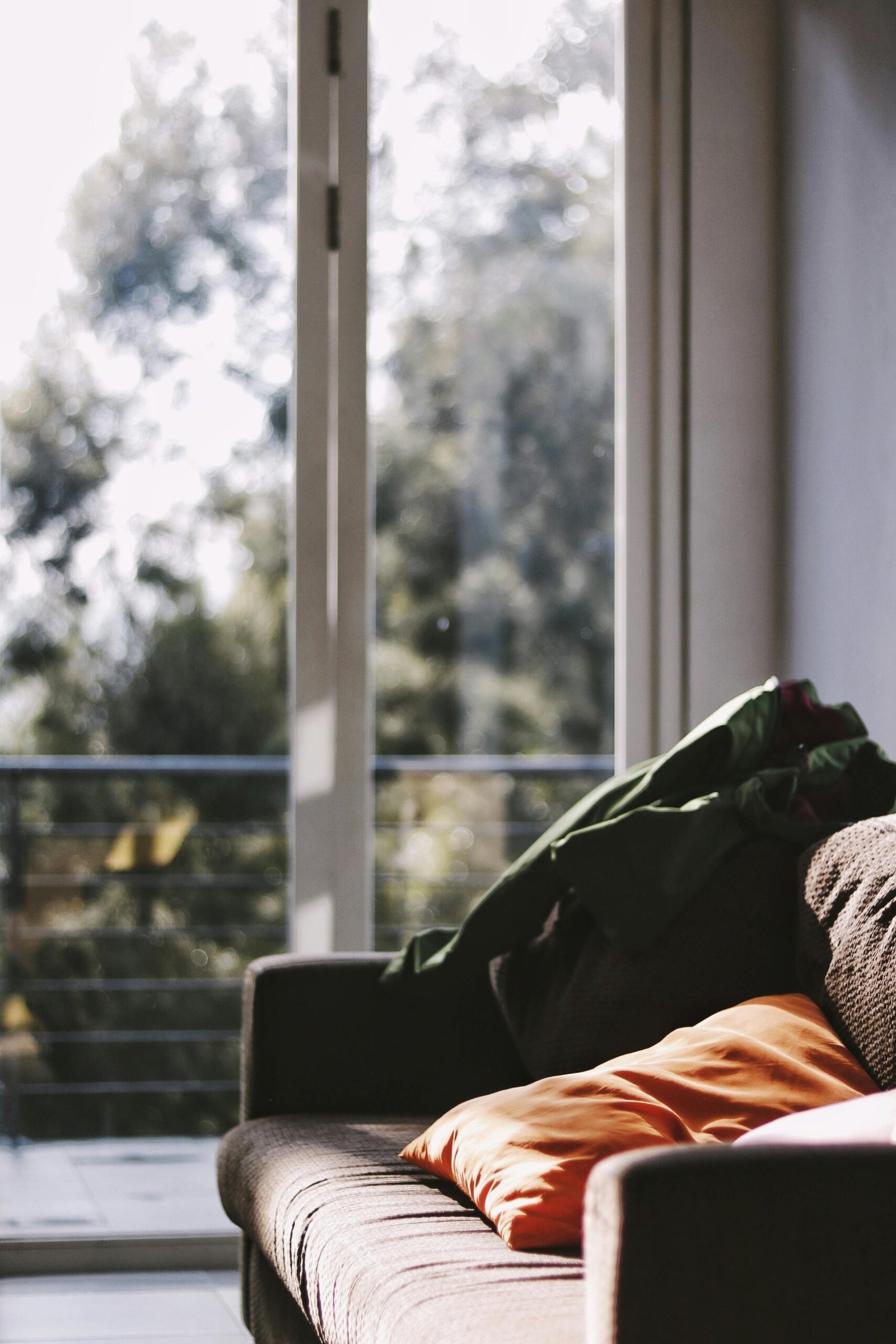 A cozy living room with sunlight streaming through sliding doors and soft cushions on a sofa.