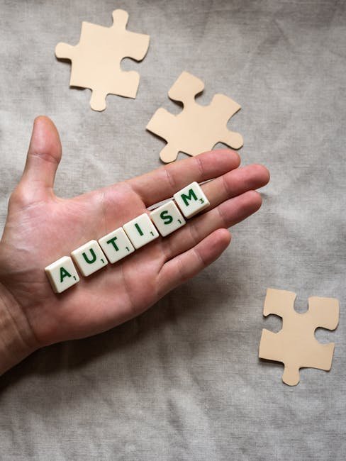 Conceptual image showing a hand holding 'autism' tiles among puzzle pieces, signifying autism awareness.