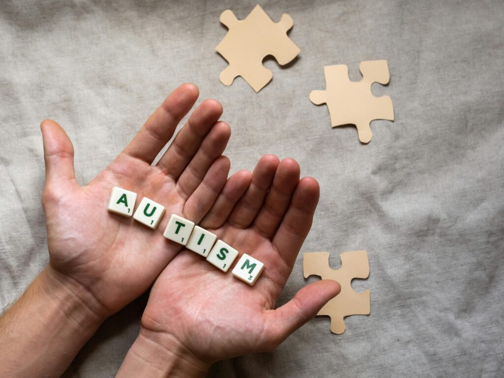 Close-up of hands with autism awareness message on Scrabble tiles and puzzle pieces on fabric.